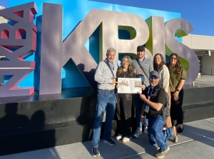 Edmond Kitchen and bath employees in front of the KBIS sign at the Kitchen and Bath Industry Show in Las Vegas, holding the magazine with their work inside.